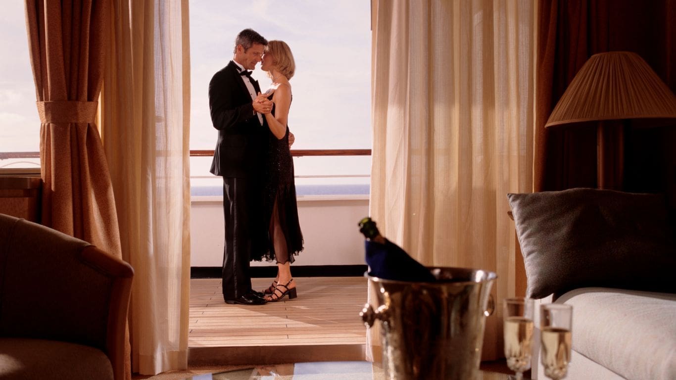 A couple shares an intimate dance on a sunlit cruise balcony, a bottle of champagne chilling nearby, creating a romantic and elegant atmosphere.