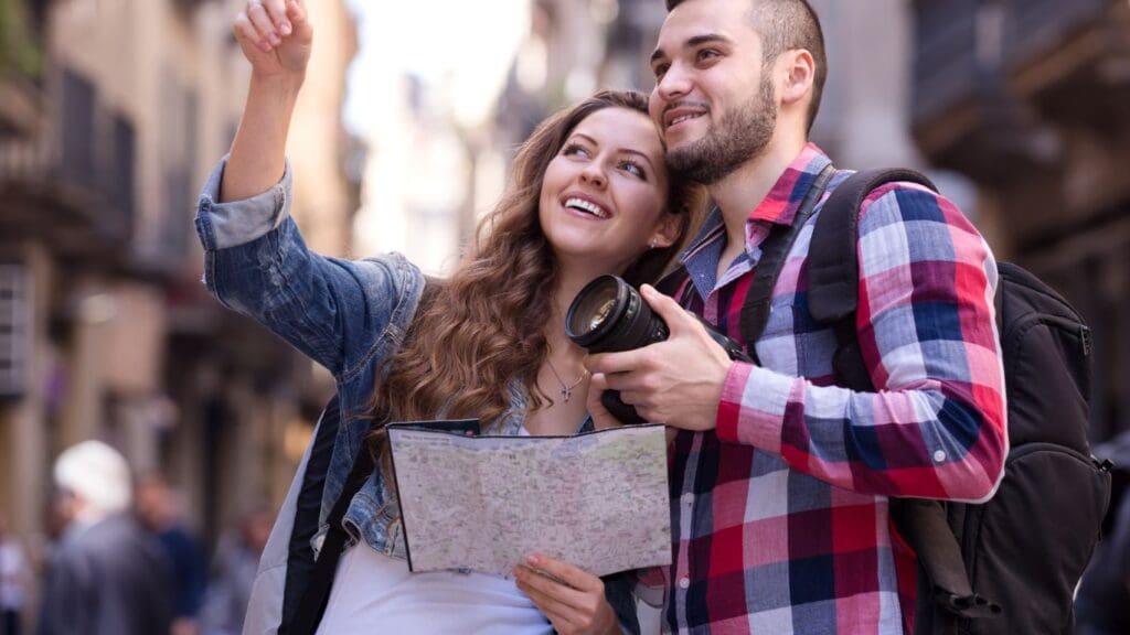 A couple happily explores a charming city street, using a map and camera to capture memories of their travel adventure while on a cruise.