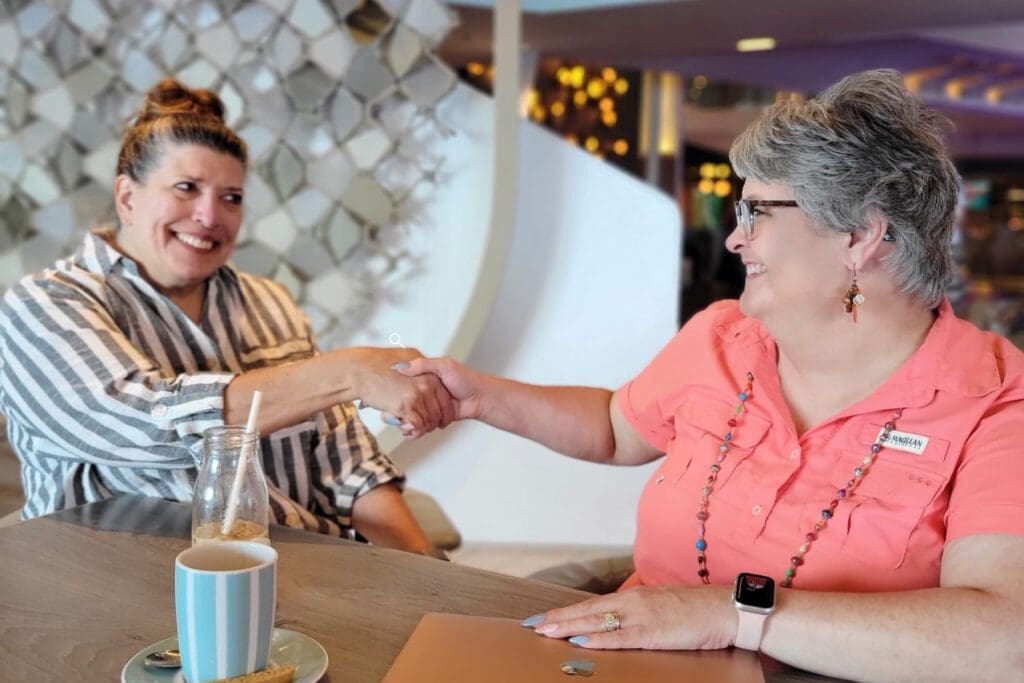Carri Arman meeting with a client on a cruise ship, shaking hands during a personal travel planning conversation.
